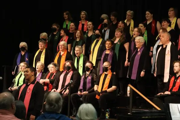 A closer view of Confluence: Willamette Valley LGBT Chorus singing during a concert. Chorus members in black clothing and brightly colored scarves perform together on stage, representing a diverse and multigenerational LGBTQ+ community and its allies.