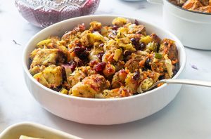 Savory holiday stuffing with toasted bread, cranberries, vegetables, and herbs in a white serving bowl.